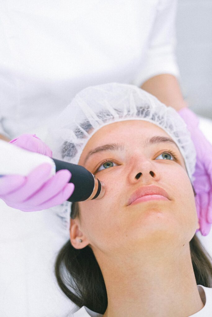 Close-up of a woman receiving a laser facial treatment by an aesthetician with protective gloves.