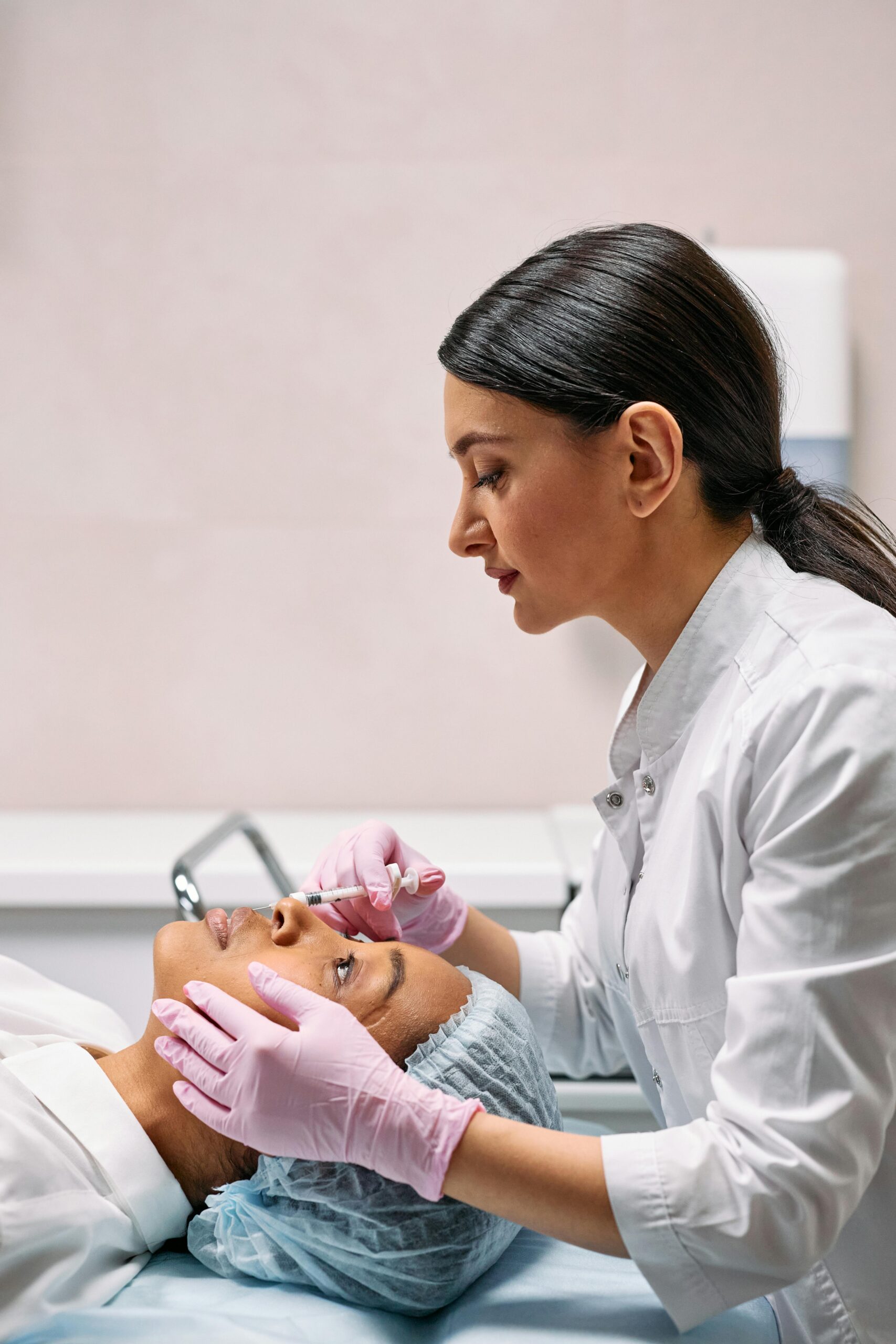 A female dermatologist applying a facial treatment to a patient in a medical clinic setting.